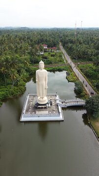 Aerial view of the Tsunami Honganji Viharaya standing Buddha statue surrounded by lush palm trees and a pond in Peraliya, Southern Province, Sri Lanka.