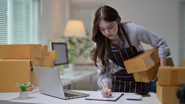 Online seller working on laptop and taking notes of orders