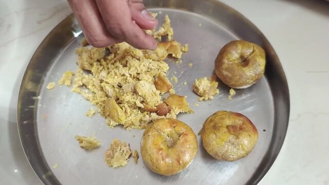 Hand crushing roasted wheat baati into fine crumbles on a steel plate close up