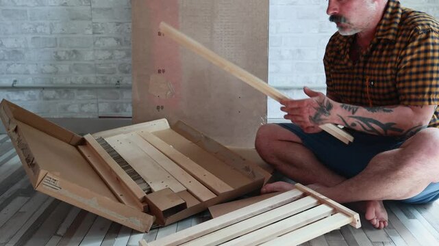 Tattooed man assembling flat pack furniture at home