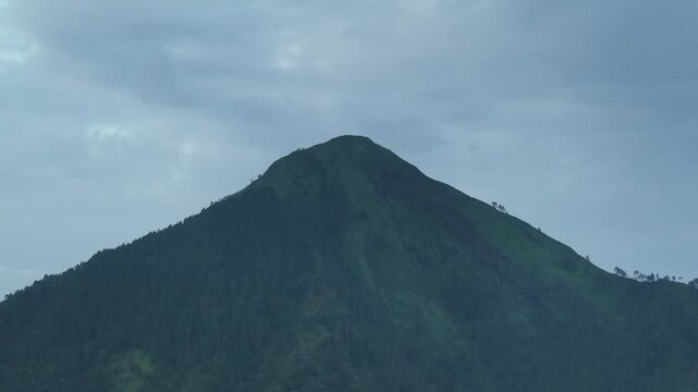Aerial view of a lush green mountain peak under a cloudy sky in Kecamatan Ngablak, Jawa Tengah, Indonesia.