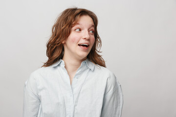 Obraz premium Young woman with curly hair wearing white shirt looks surprised and happy against light background. Concept of positive emotions, casual style, and natural beauty in studio portrait.