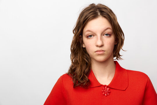 Young woman with brown hair wearing red sweater looks tired and indifferent on white background. Concept of fatigue, boredom, and emotional exhaustion in everyday life.