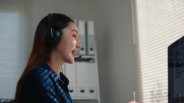Happy asian telemarketing agent wearing a headset with microphone working in a call center, providing positive customer service
