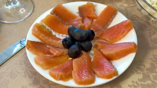 Red trout slices with olives plated on white porcelain plate arranged in floral pattern with light salt sprinkle beside vintage