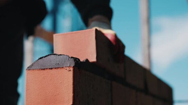 Worker laying facing brick on mortar during wall construction