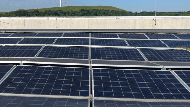 Solar panels installed on a rooftop with a green hillside in the background, for renewable energy and sustainability content, solar power and clean technology visuals, vertical photo