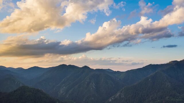 Clouds float across the blue sky with sunlight over the valley of the Rhodope Mountains with spruce forests