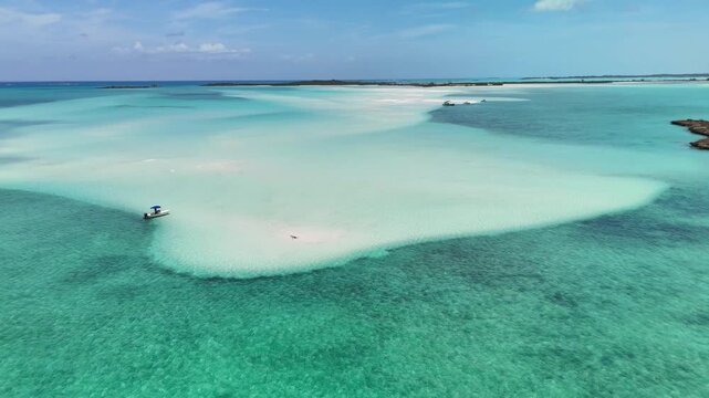 Aerial view of Man-O-War Cay Sandbar with a small boat anchored in turquoise waters near Rolletown, Exuma, The Bahamas.