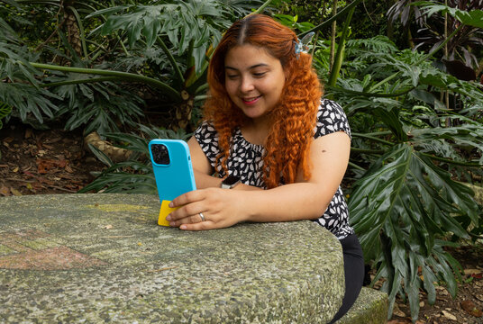 Freckled young woman sitting at a park table attentively looking at her mobile phone. Entertainment, digital communication, social media, and leisure time concept