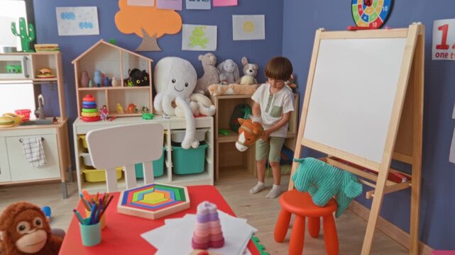Boy holding a plush horse by a storage shelf in a playroom inside a building near an easel and octopus plush; playful curiosity.
