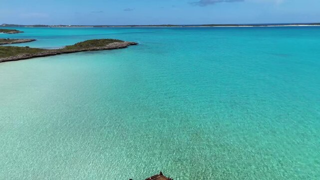 Aerial view of the crystal clear turquoise waters surrounding Crab Cay with lush green vegetation under a blue sky in George Town, Exuma, The Bahamas.