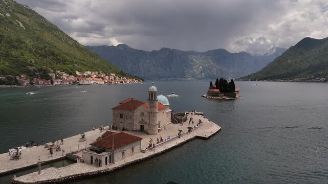 Our Lady of the Rocks Montenegro 4K Aerial Video, Wide Angle Drone Pull Back over Perast Artificial Island with Tourists, Boats, and Mountain Fjord Backdrop