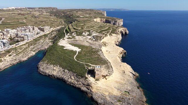 Aerial view of the historic Xlendi Tower standing on a rocky peninsula overlooking the blue Mediterranean Sea and coastal cliffs in Munxar, Gozo Region, Malta.