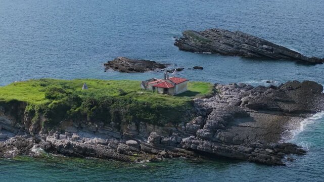 Solitary hermitage of El Carmen on a rugged island in Luanco, Asturias, with waves breaking on the rocky coast of Spain