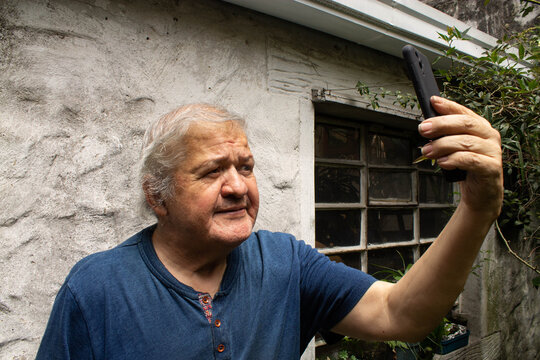 Retrato de un hombre mayor sosteniendo un tel&eacute;fono inteligente para tomarse una selfie o realizar una videollamada.