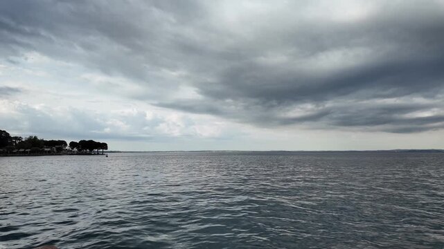 Bardolino, Italy - May 14, 2026 - Calm lake water under dramatic cloudy sky with distant treeline and shoreline
