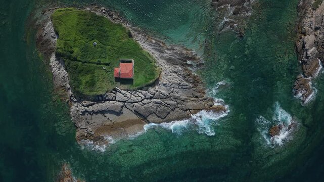 Aerial view of a lonely chapel on a rocky island in Luanco, Asturias, with turquoise ocean water and waves breaking