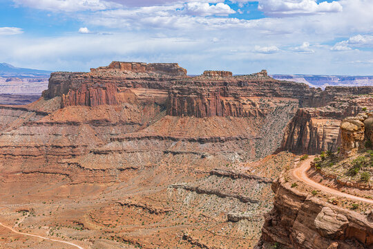 A massive layered red rock mesa dominates the view above a deep canyon at Canyonlands, with the narrow Shafer Trail visible along the canyon edge.