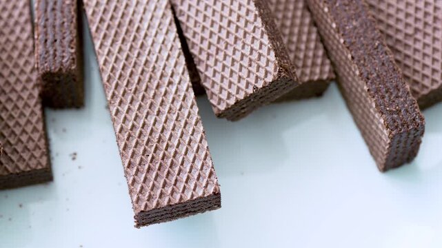 Crispy waffles with chocolate filling being taken one by one from a pile on white background, macro shot
