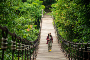 Fototapeta premium Woman Hiker Exploring A Wooden Suspension Bridge In A Lush Tropical Forest