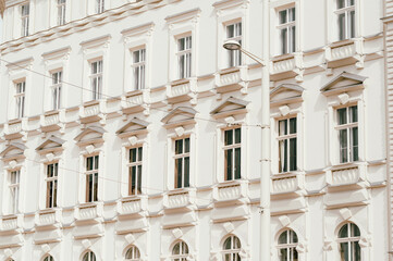 Close-framed view of a pale cream classical building facade featuring repeated windows, decorative cornices, pilasters, and balustrade-like ledges. Soft © Vulp