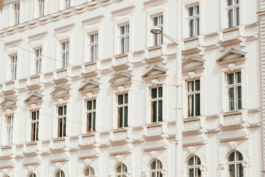 Close-framed view of a pale cream classical building facade featuring repeated windows, decorative cornices, pilasters, and balustrade-like ledges. Soft