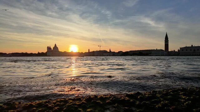 Venice Italyn scenic time-lapse of sunset over the lagoon with passing vaporetto water buses, ferry and a seagull in foreground.