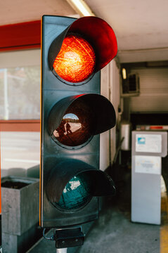 Vertical close-up of a three-lens traffic signal showing the top red light illuminated. The metal housing and visors are visible, with reflections in the