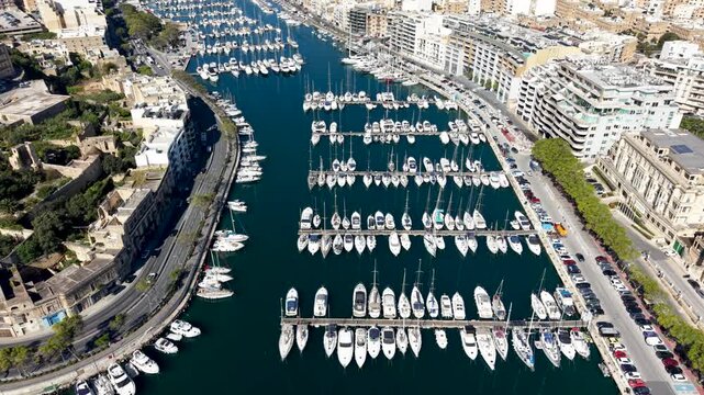Aerial view of numerous yachts and boats docked in the Msida Marina with waterfront buildings and parked cars in Ta' Xbiex, Eastern Region, Malta.