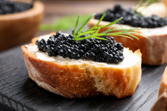 Delicious bruschettas with black caviar on wooden board, closeup
