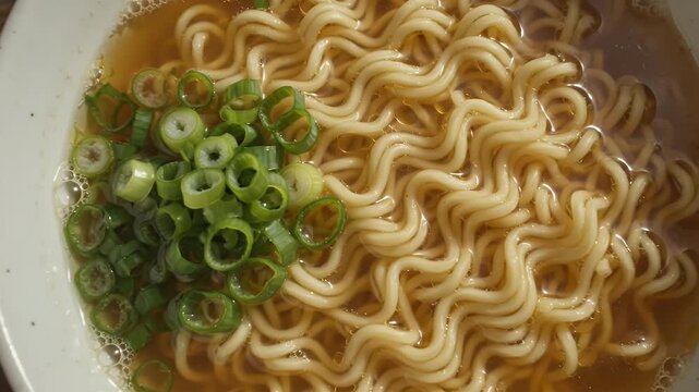 A bowl of hot instant ramen noodles with chopped green onions on a rustic wooden table