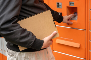 Man holding cardboard box entering PIN code on parcel locker keyboard. Receiving and sending parcels in an automated terminal © Gereish