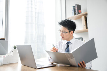 Fototapeta premium Young businessman reviewing documents at laptop in bright modern office