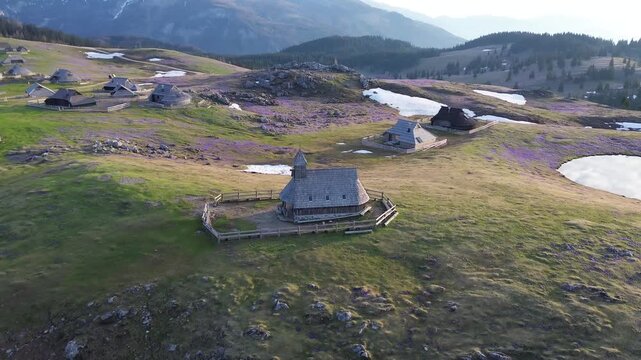 Aerial drone panorama of Velika Planina wooden chapel and traditional herdsmen village at sunrise in spring, Slovenia