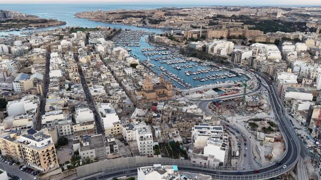 Aerial view of the historic Msida Parish Church and the yacht marina surrounded by dense urban architecture and modern road infrastructure in Msida, Eastern Region, Malta.