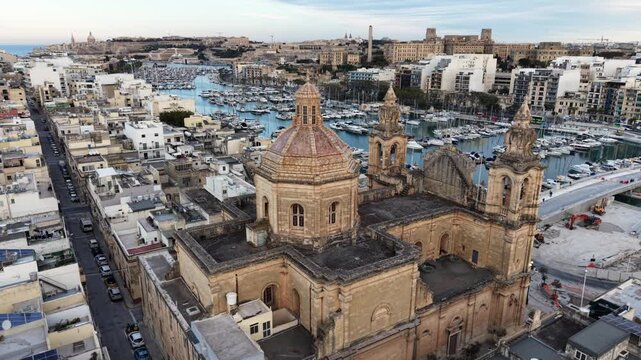Aerial view of the historic St. Joseph's Parish Church with its large dome and bell towers overlooking the yacht marina and urban rooftops in Msida, Eastern Region, Malta.
