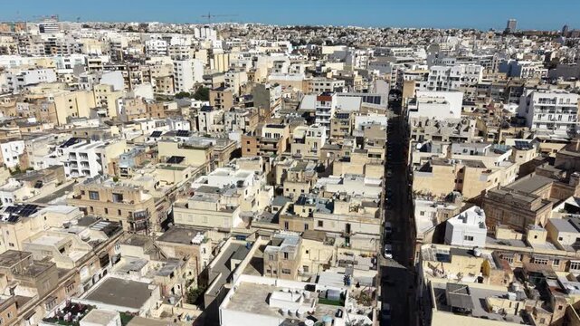 Aerial view of the dense urban landscape with traditional limestone buildings, flat rooftops, and narrow streets under a clear blue sky in Msida, Eastern Region, Malta.