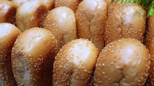 Close up of sesame seed burger buns arranged in rows. Warm golden brown rolls with toasted tops filling the frame.