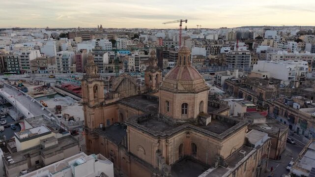 Aerial view of the historic St. Joseph Parish Church featuring its dome and twin bell towers amidst the urban landscape of Msida, Eastern Region, Malta.