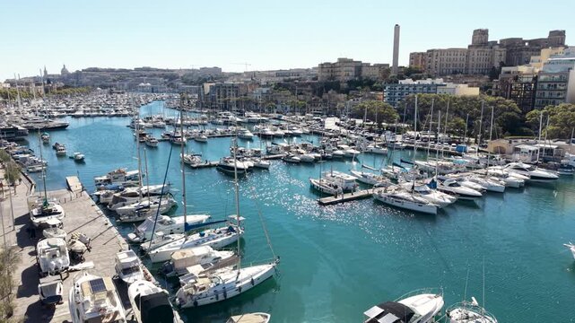 Aerial view of numerous yachts and sailboats docked in the Msida Marina under a clear blue sky with urban buildings in the background, Msida, Eastern Region, Malta.