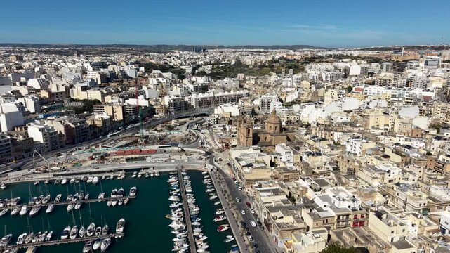 Aerial view of the Msida Parish Church overlooking the yacht marina with rows of boats and dense urban architecture under a clear blue sky in Msida, Eastern Region, Malta.