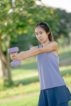 A woman is lifting dumbbells in a park and exercising.