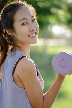 A woman is lifting dumbbells in a park and exercising.