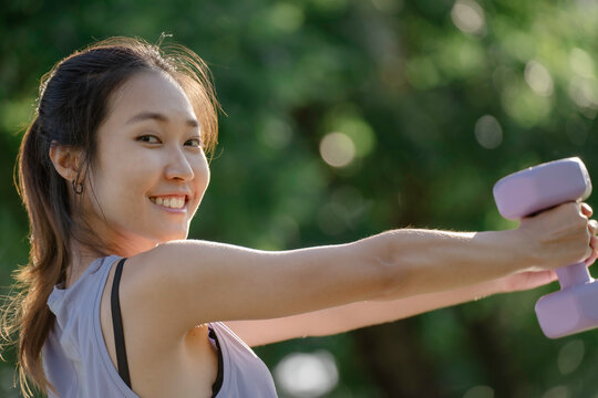 A woman is lifting dumbbells in a park and exercising.