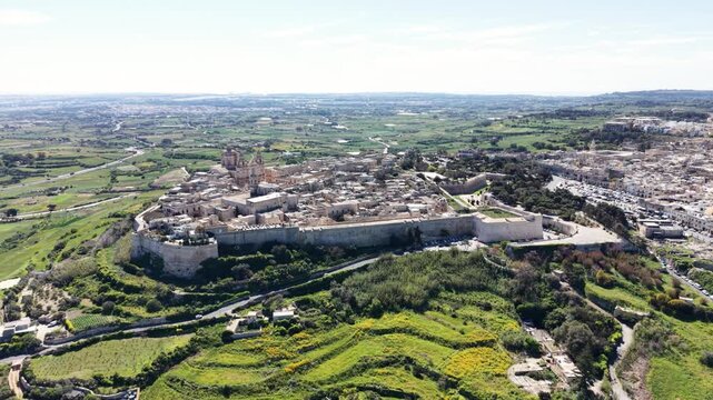 Aerial view of the historic fortified city of Mdina with its ancient stone walls and St. Paul's Cathedral surrounded by green fields in Mdina, Western Region, Malta.