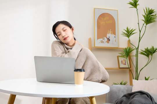 Young woman relieving neck pain while working on laptop at home