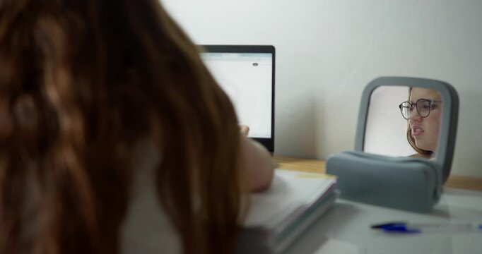 Mirror of Reflection: A young person with long, wavy hair sits at a desk, engrossed in their laptop. A mirror reflects their frustrated expression.