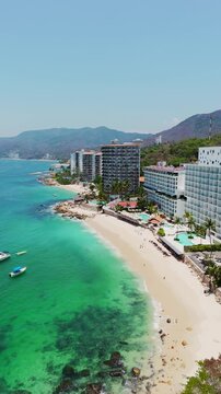 Aerial view of Las Gemelas Beach with luxury hotel resorts along the turquoise coastline and lush green hills in Puerto Vallarta, Jalisco, Mexico.