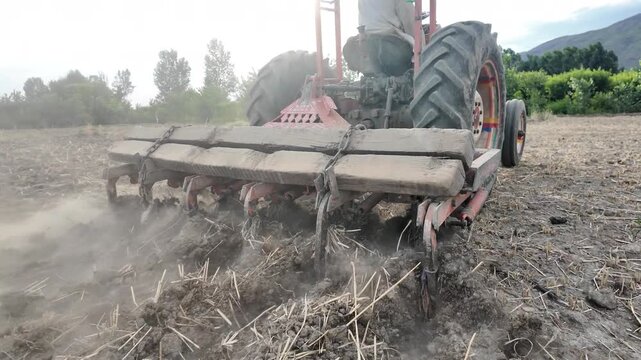Slow motion tractor plowing fields with cultivator, turning soil for planting


